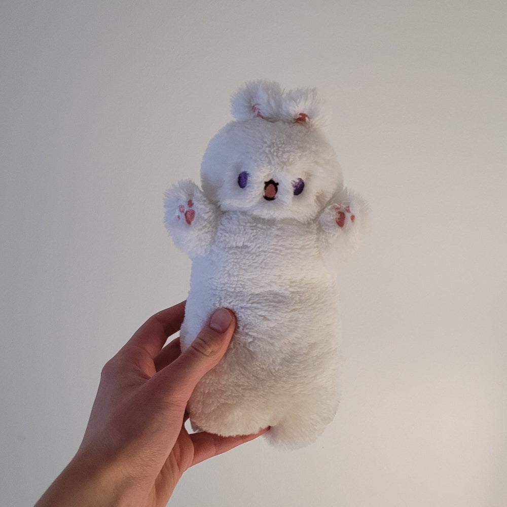 White plush toy resembling a bunny held by a hand against a plain background