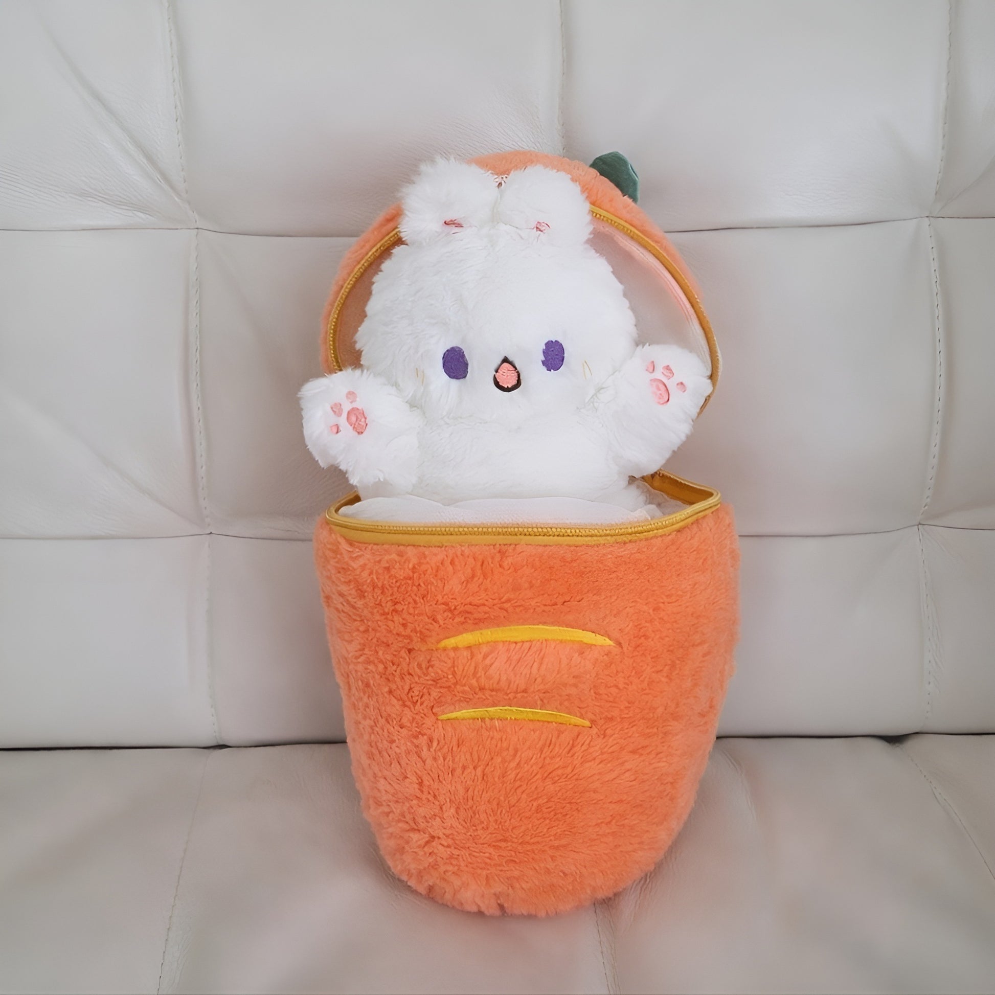White plush toy with purple eyes and pink nose peeking out from an orange plush bag on a light-colored couch.
